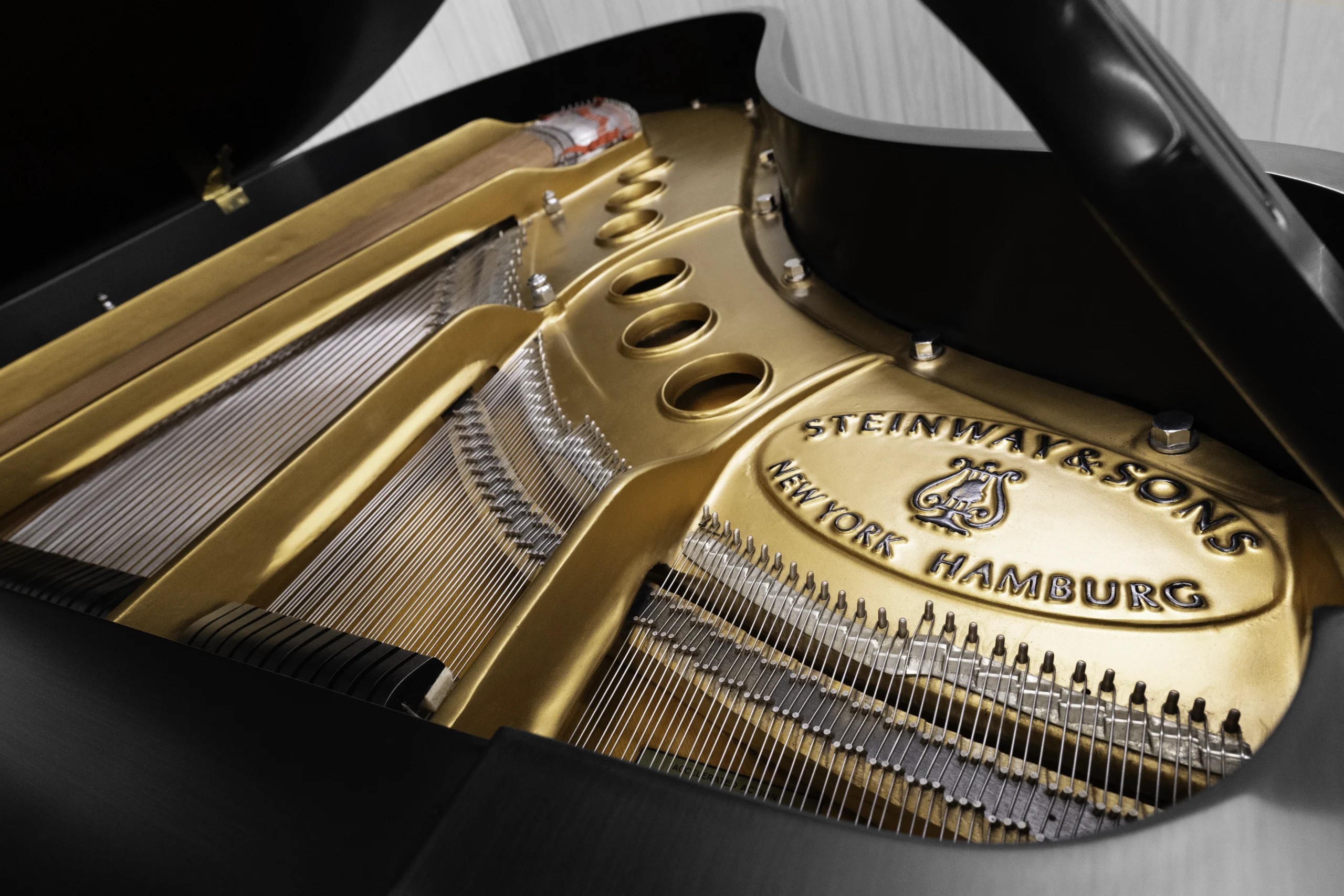 A Steinway M baby grand piano in a beautiful satin ebony finish with brass hardware and a bench. The image shows off the interior of the piano including the harp and strings.