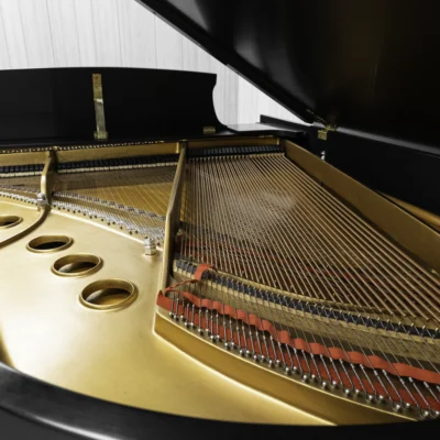 A Steinway M baby grand piano in a beautiful satin ebony finish with brass hardware and a bench. The image shows off the interior of the piano including the harp and strings.