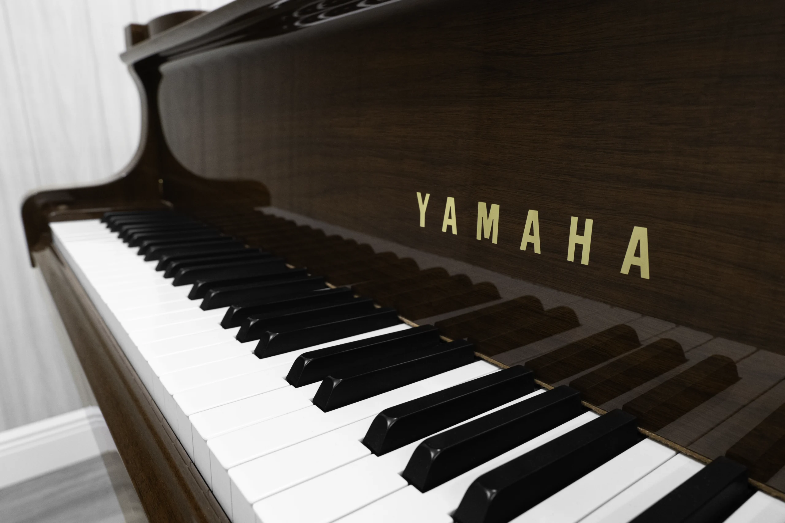 A Yamaha G1 piano in a beautiful mahogany finish with brass hardware. This image shows off the keys and fallboard logo.