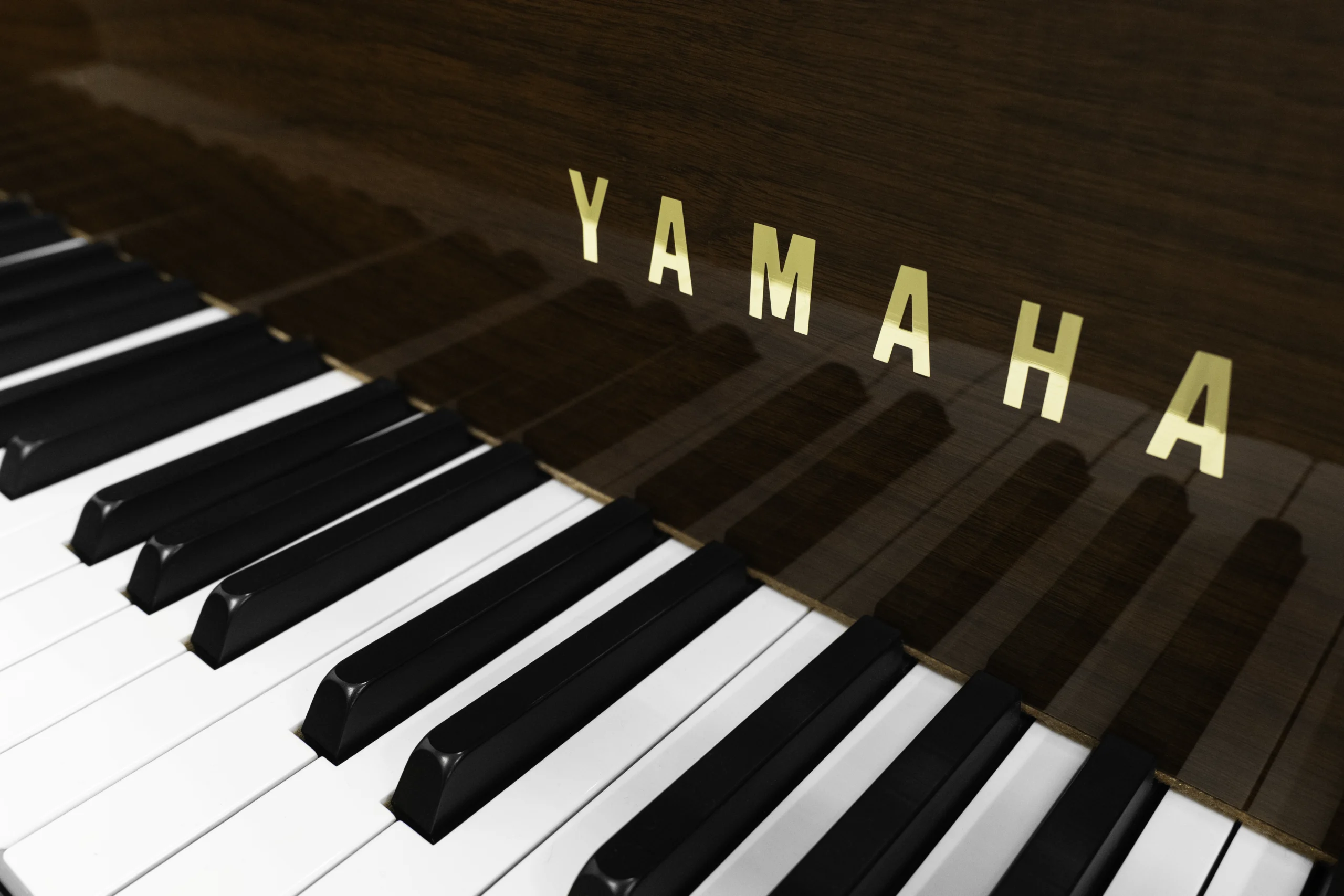 A Yamaha G1 piano in a beautiful mahogany finish with brass hardware. This image shows off the keys and fallboard logo.